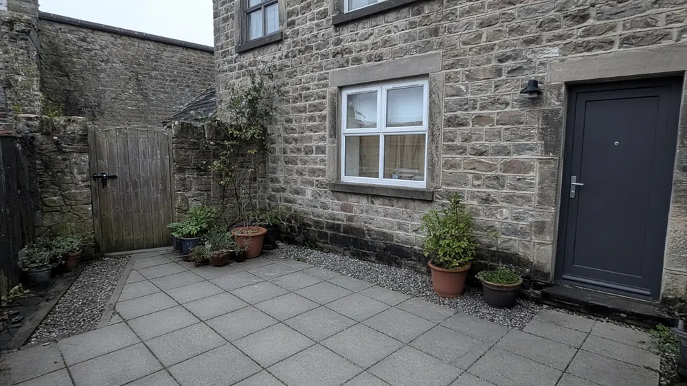 Example image: grey slab patio with a gravel strip along the house wall behind a terraced cottage