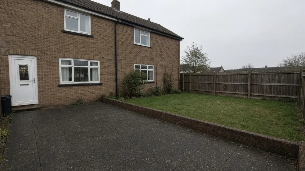 Example image: charcoal slab patio with a low brick edge behind a 1980s detached house